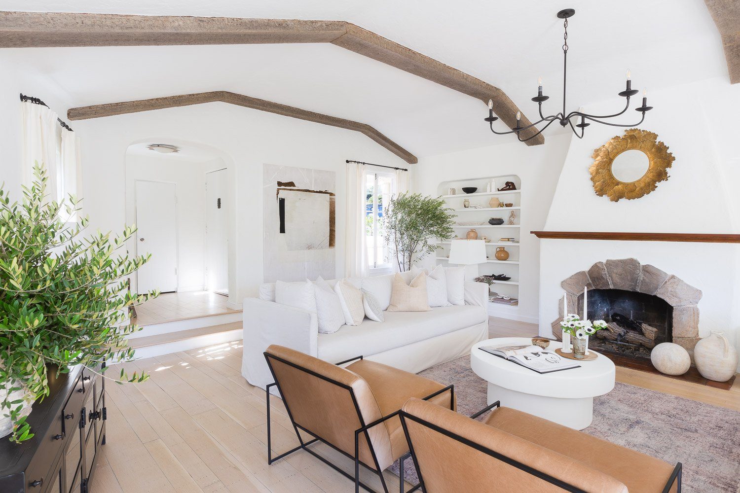 Furnished great room by Saga Interiors with a vaulted beamed ceiling, stone fireplace and white sofa