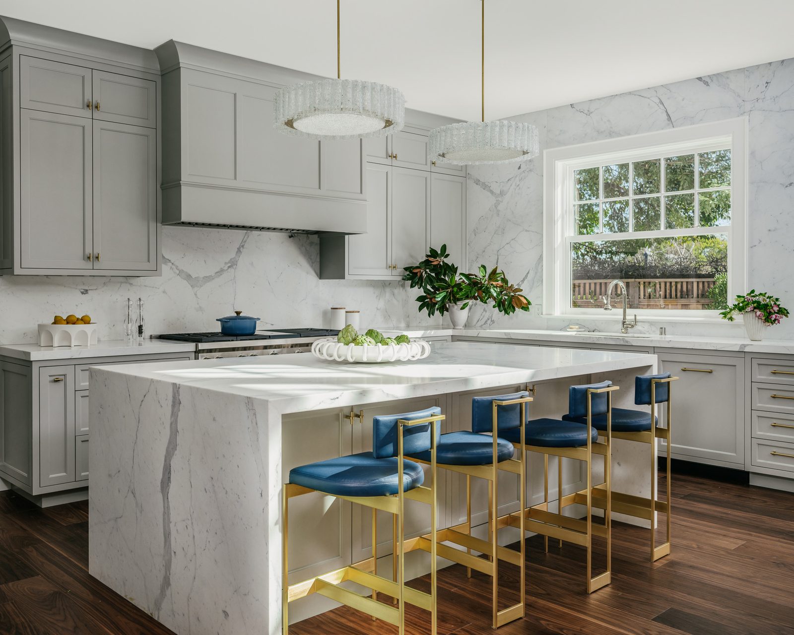 Kitchen by Tineke Triggs Interiors with a book-matched marble waterfall island and blue velvet counter stools